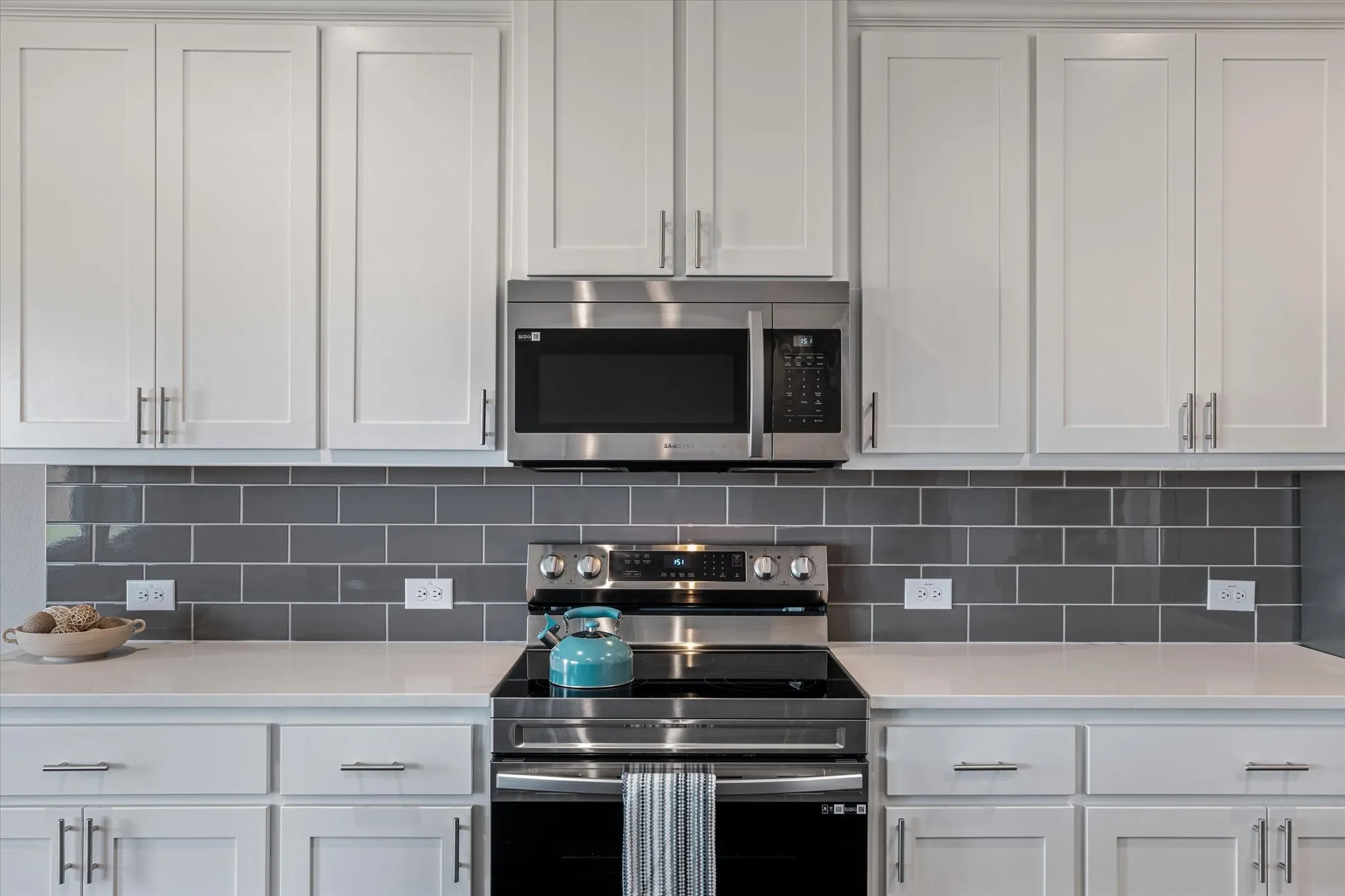 White shaker-style cabinetry, stainless steel appliances, solid surface countertops, and a gray subway tile backsplash
