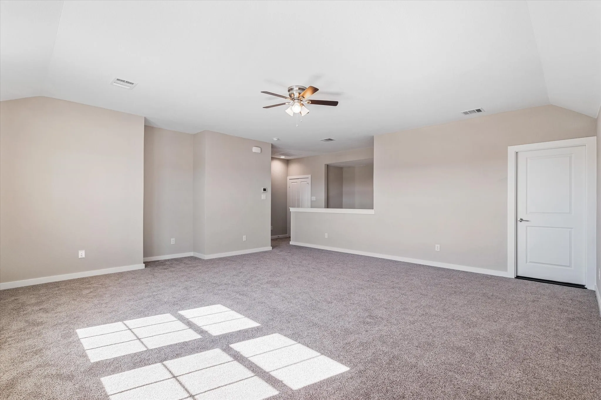 Expansive carpeted area with vaulted ceilings, a ceiling fan, and light-toned walls