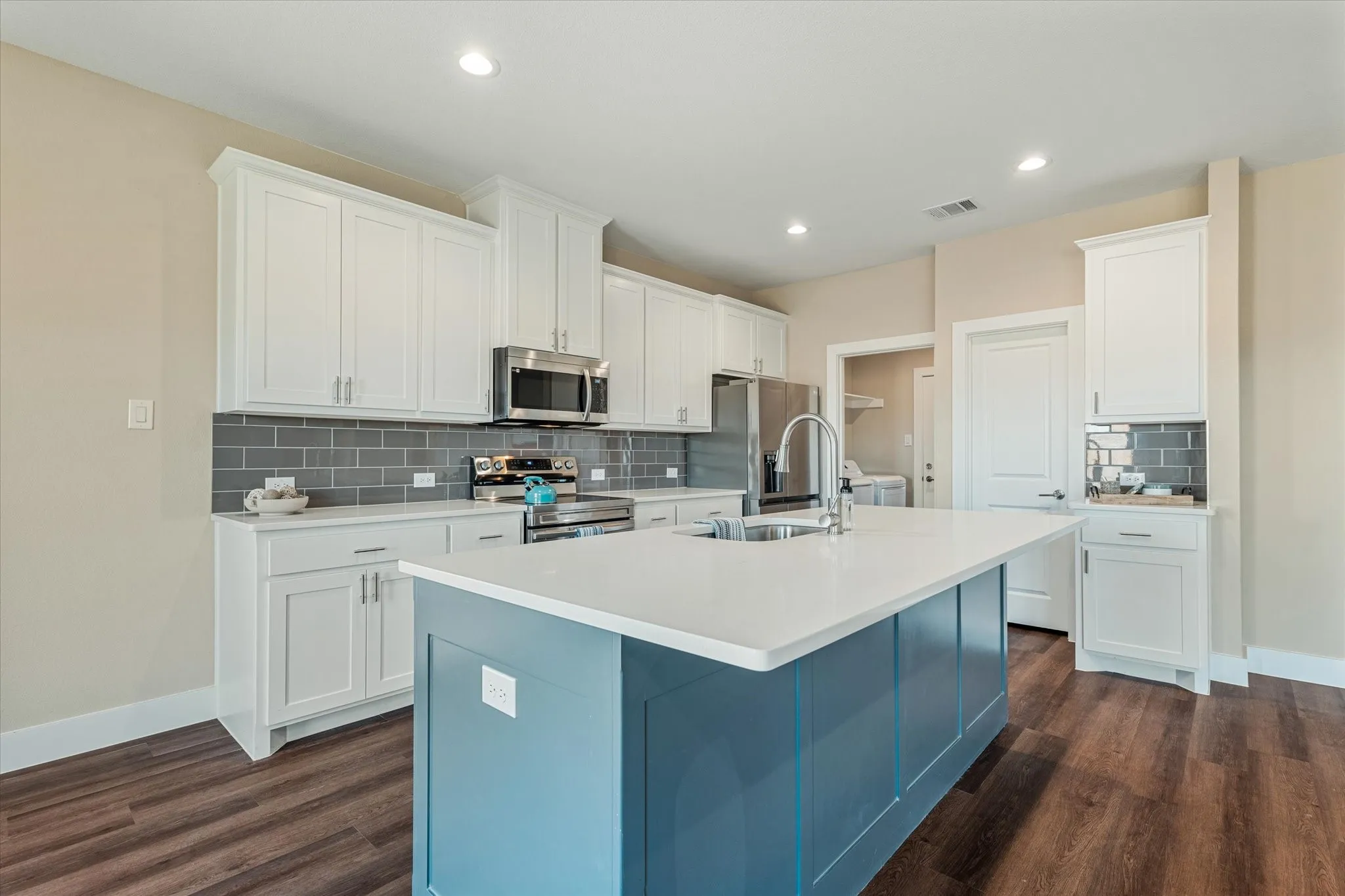 Kitchen with a central island, white shaker cabinetry, stainless steel appliances, a gray subway tile backsplash, and wood-finish flooring