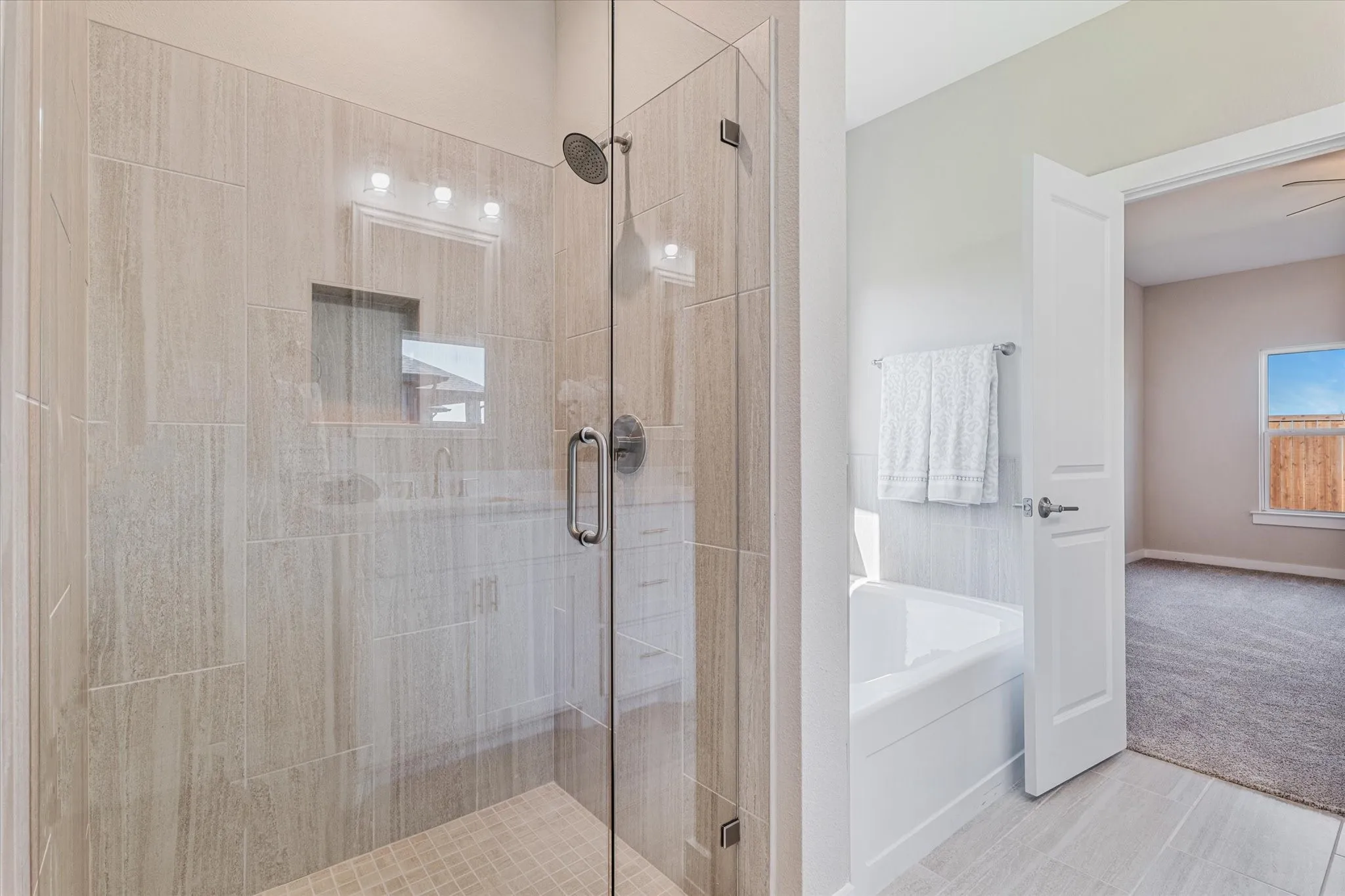 Glass-enclosed shower with tiled walls and floor, built-in shower niche, and an adjacent built-in bathtub