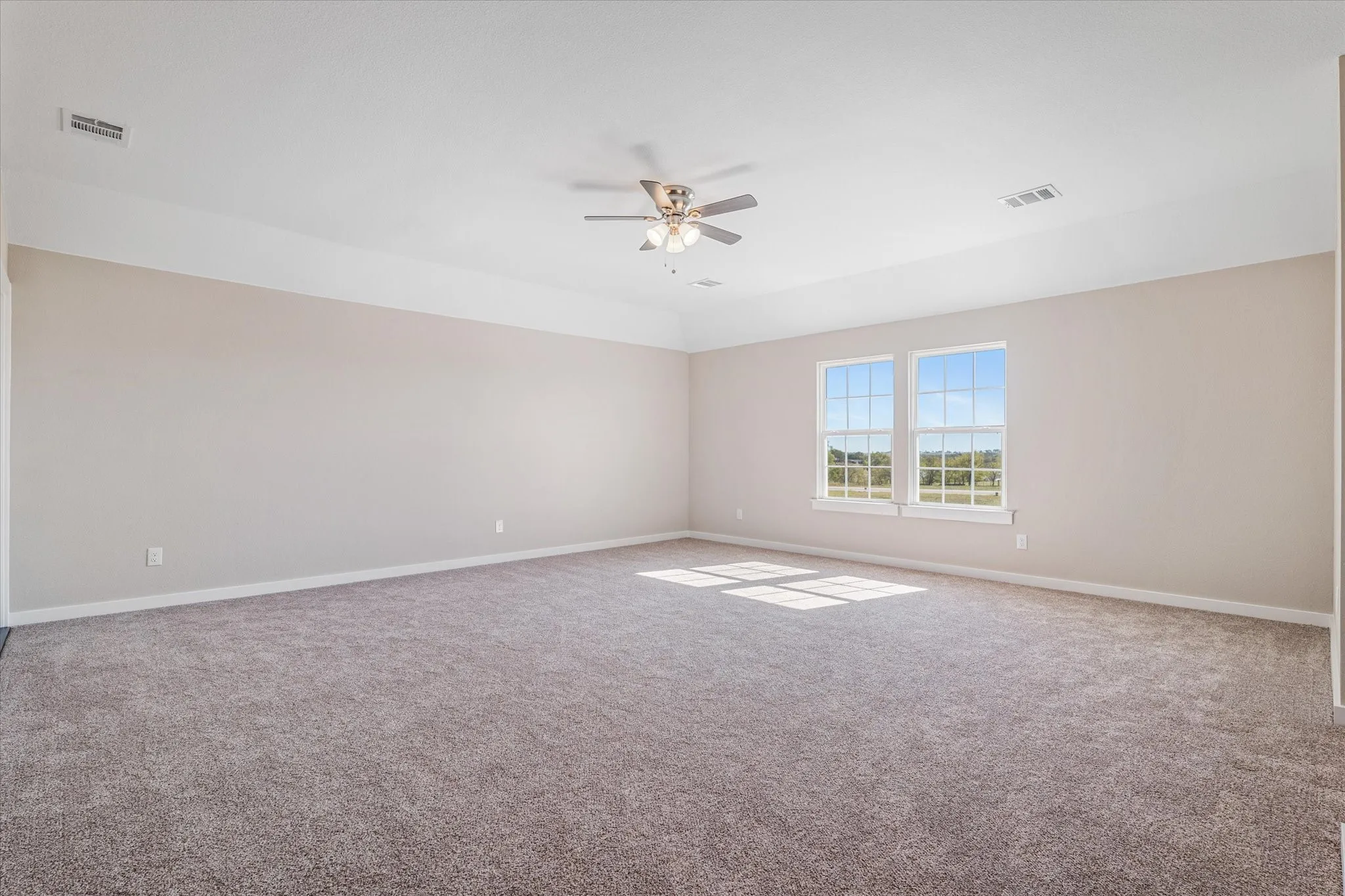 Carpeted room featuring a tray ceiling, ceiling fan, and two windows