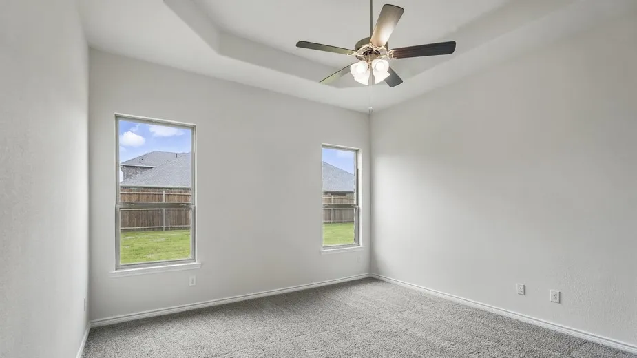Spacious room featuring a tray ceiling, ceiling fan with integrated lighting, and neutral wall paint