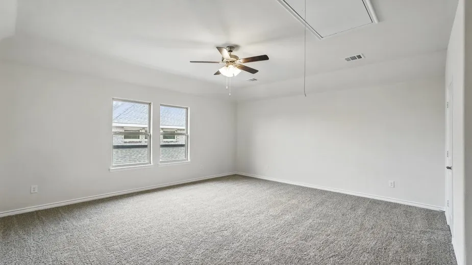 Spacious room with plush gray carpeting, two large windows, a ceiling fan with light fixture, and an attic access panel