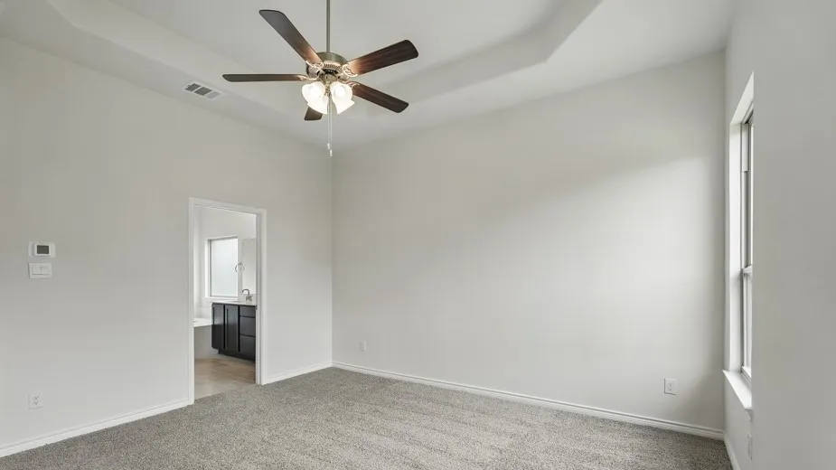 Spacious room featuring gray carpeting, a tray ceiling, and a ceiling fan with integrated lighting