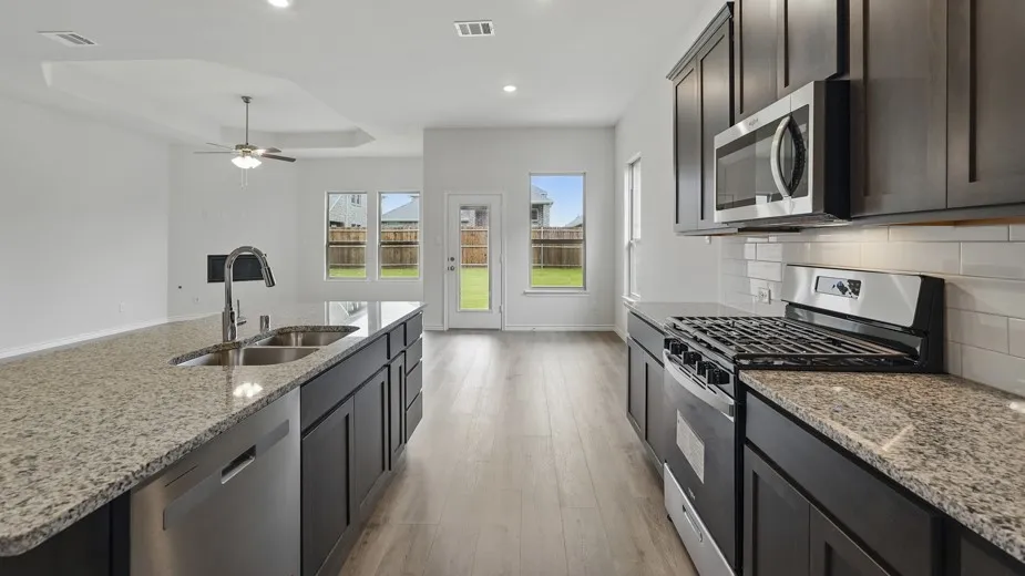 Modern kitchen featuring granite countertops, dark wood-finish cabinetry, stainless steel appliances, and a subway tile backsplash