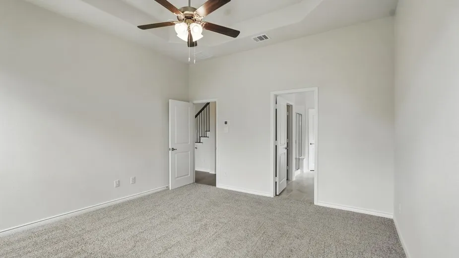 Spacious carpeted room featuring a tray ceiling with a ceiling fan, white paneled doors, and light-colored walls