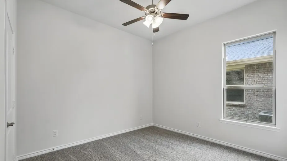 Interior room featuring light-colored walls, grey carpeting, a ceiling fan with integrated lighting, and a white-framed window