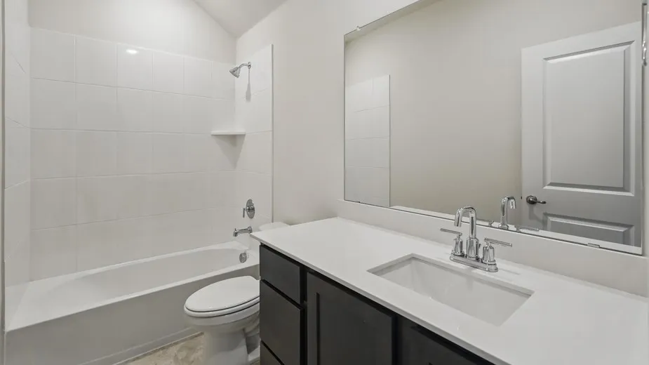 Contemporary bathroom featuring a dark wood-finish vanity with a white countertop and integrated sink, a large wall-mounted mirror, and a white tiled shower/tub combination
