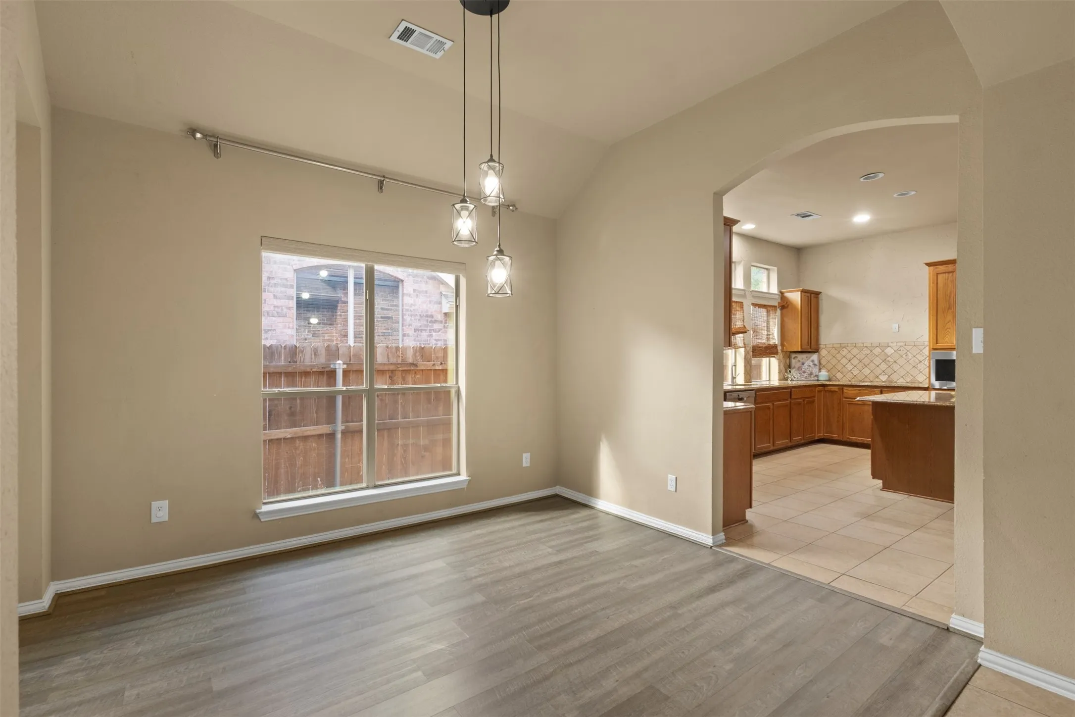Vaulted ceiling with a contemporary pendant light fixture, wood-finish flooring, and an arched doorway leading to a kitchen with tile flooring