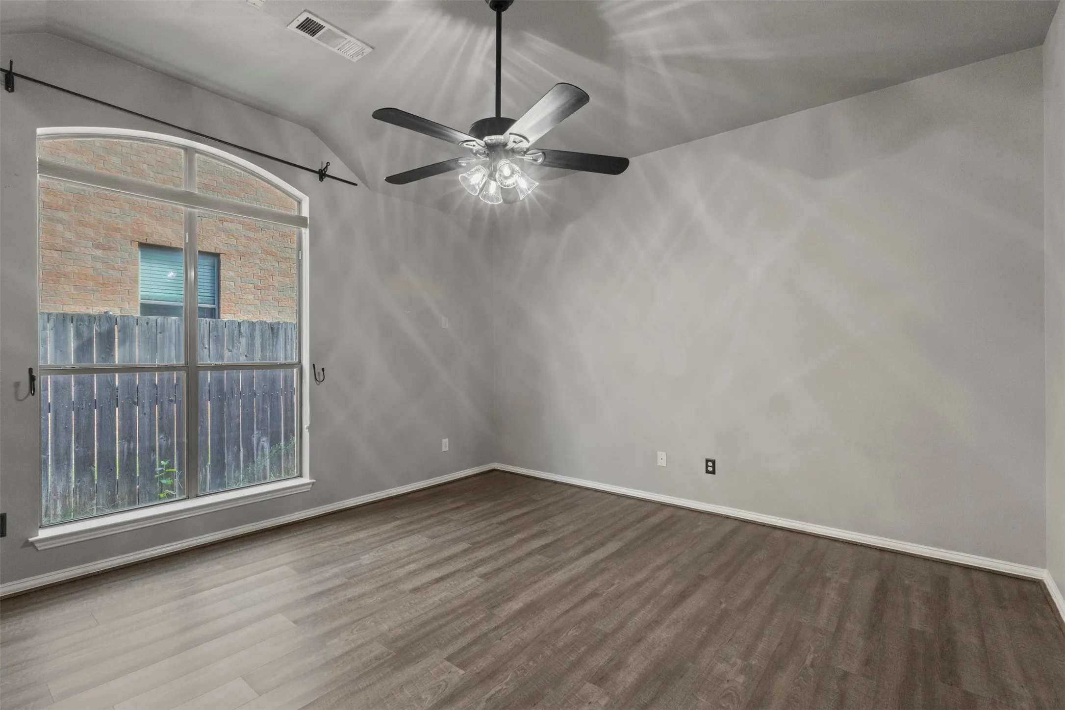 Arched window with transom, wood-finish flooring, ceiling fan with integrated lighting, and neutral wall tones