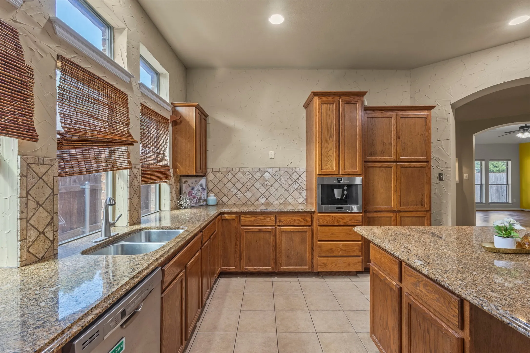 Kitchen featuring wood-finish cabinetry, stone countertops, tiled flooring, stainless steel dishwasher, and built-in coffee system
