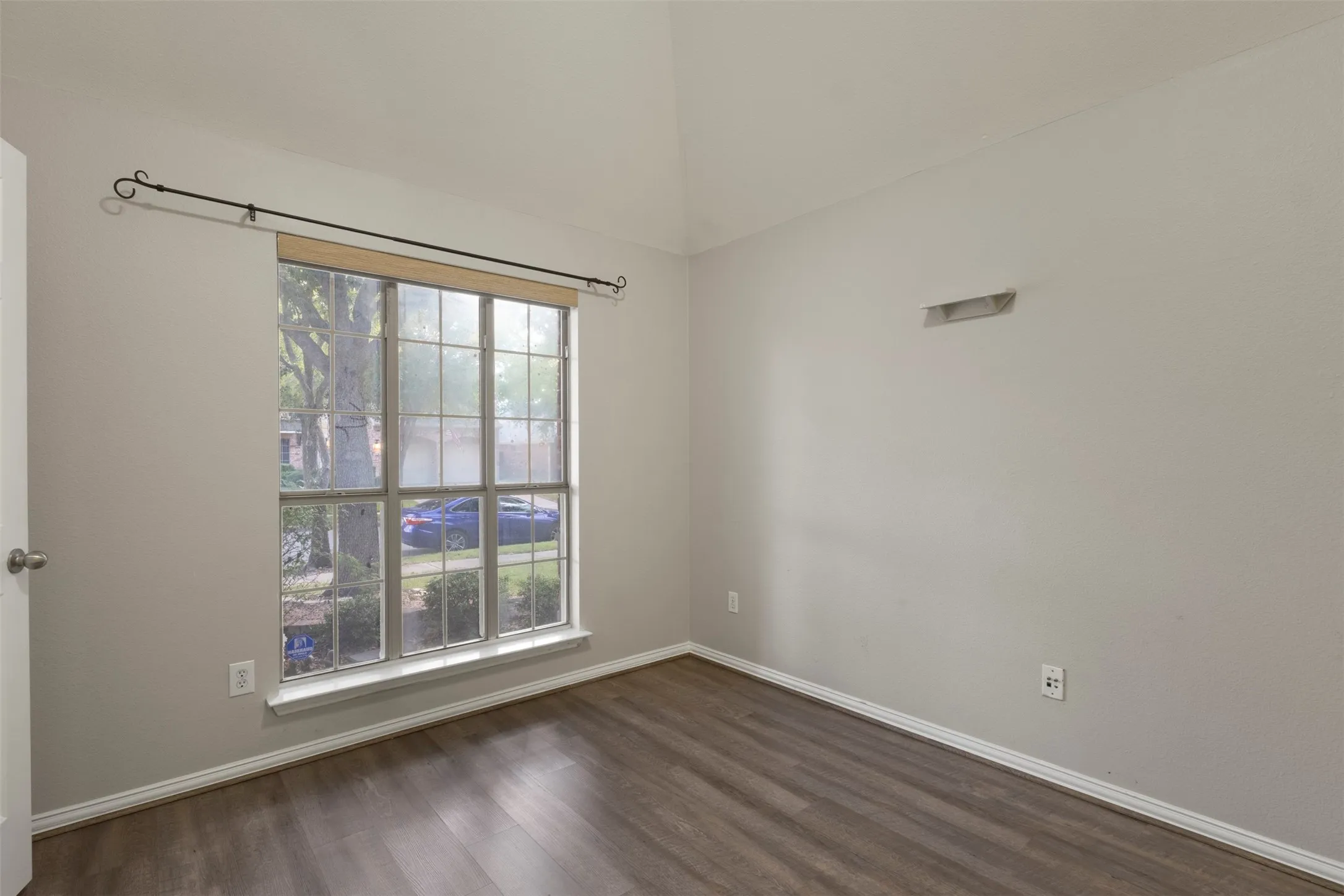 Vaulted ceiling, wood-finish flooring, white trim, and a multi-pane window