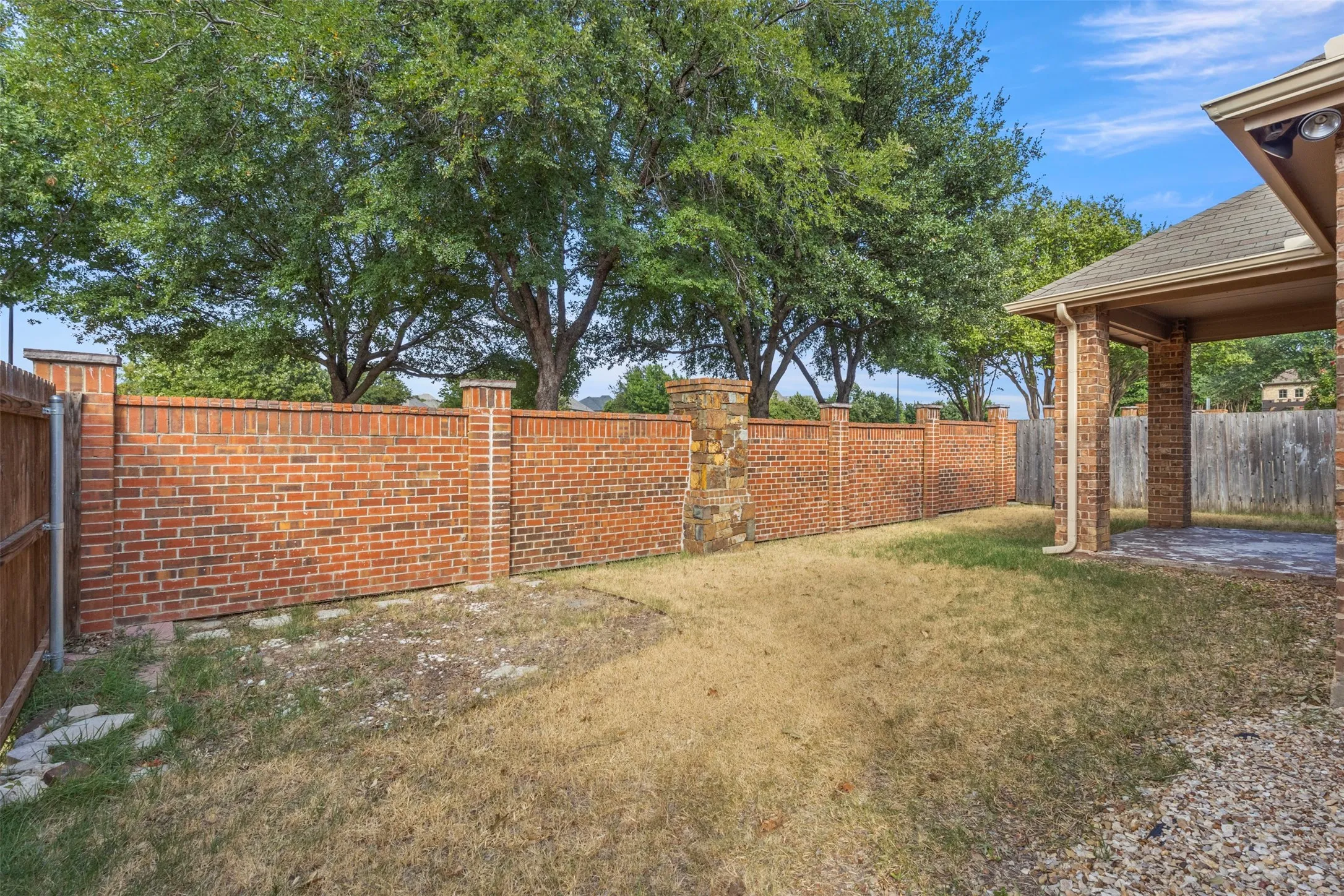 Backyard featuring a brick privacy wall with stone accents, a covered patio with brick columns, and a gravel-covered area