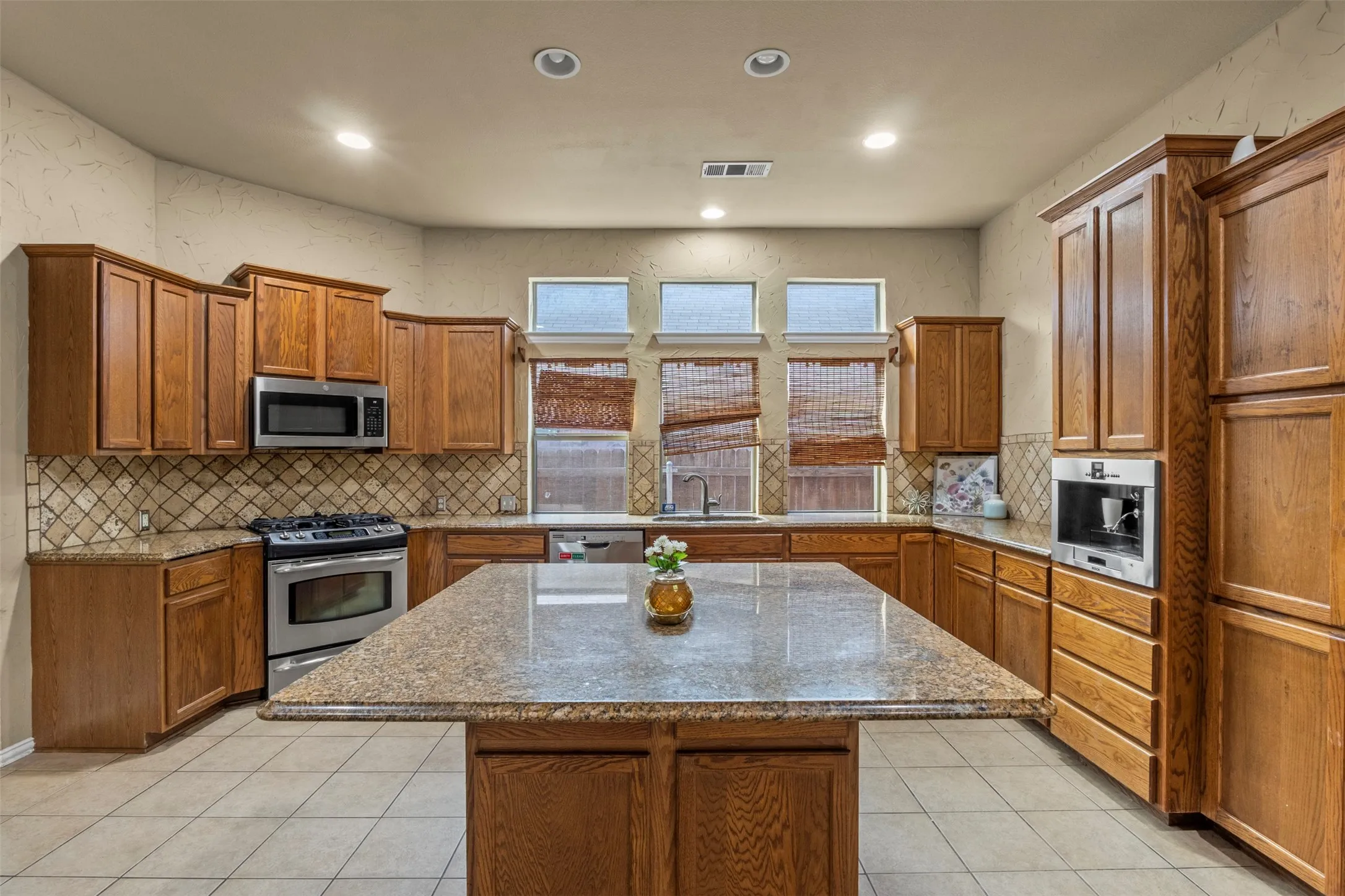 Spacious kitchen featuring an expansive central island, abundant wood cabinetry, stainless steel appliances, and tile flooring