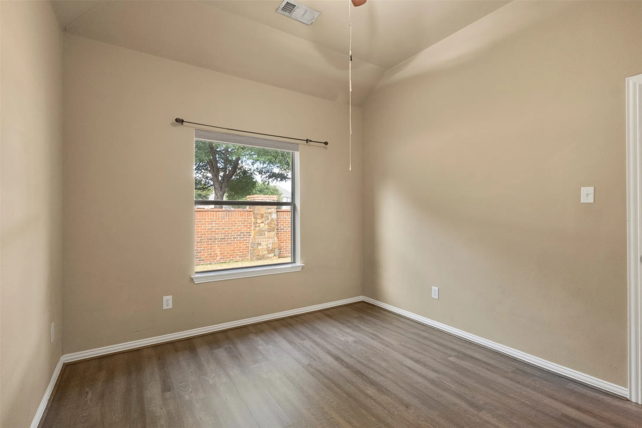 Vaulted ceiling with a ceiling fan, window with a curtain rod, wood-finish flooring, and neutral wall tones