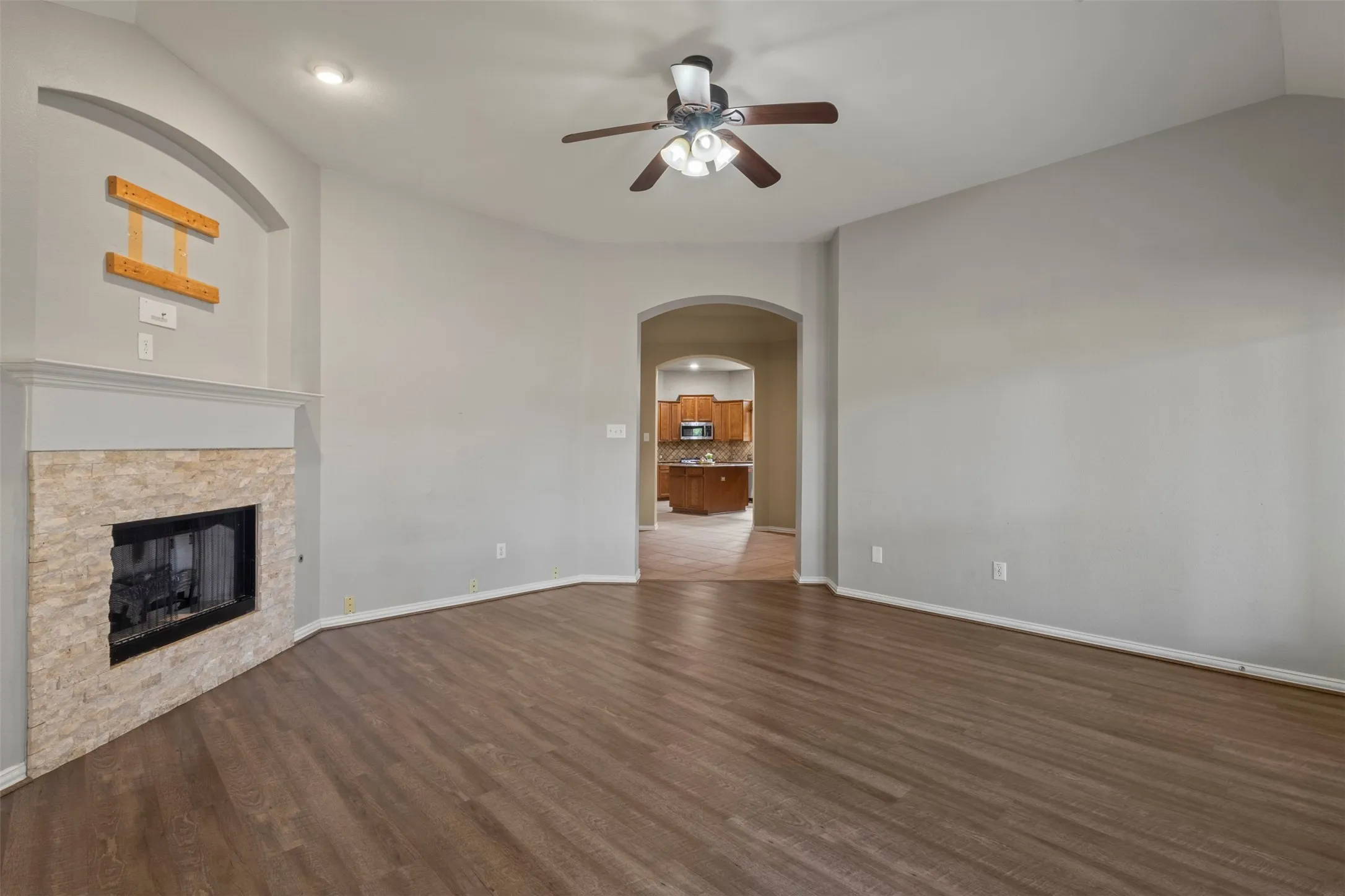 Living area featuring wood-finish flooring, a stone-clad fireplace, vaulted ceiling, recessed lighting, and a ceiling fan with light fixture