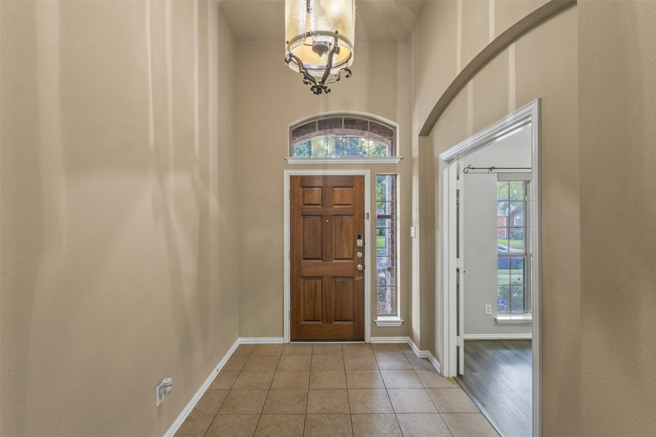 Two-story foyer with a natural wood paneled door, arched transom window, and sidelights