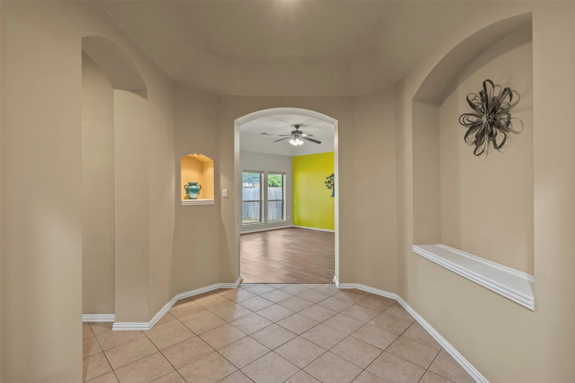 Tiled flooring with contrasting baseboards, arched doorways, a recessed wall niche with accent lighting, and a secondary arched wall niche