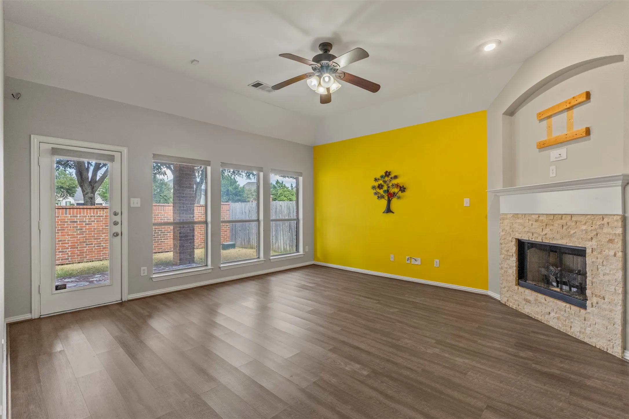 Wood-finish flooring, recessed lighting, ceiling fan, fireplace with stone surround, and multiple windows