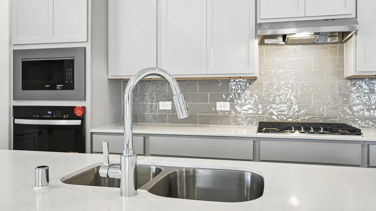 Kitchen featuring a dual basin sink with a gooseneck faucet, white shaker cabinetry, light-toned countertops, a built-in microwave, and a gas cooktop with a stainless steel range hood