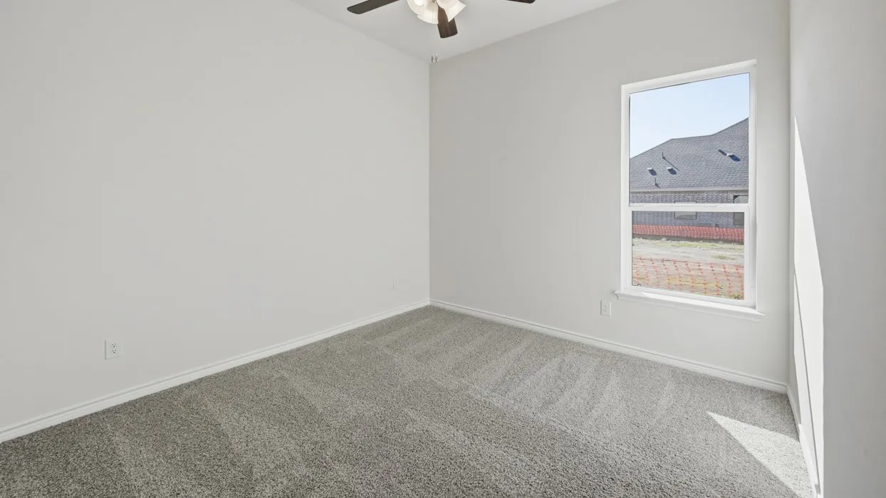 Spacious room featuring light gray carpeting, white walls, a single window, and a ceiling fan with integrated lighting