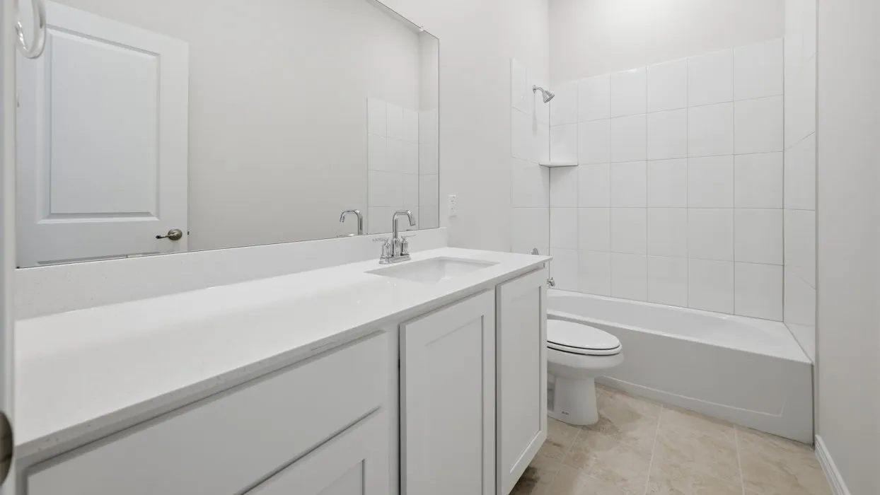 Bright bathroom featuring a single vanity with a white countertop and undermount sink, a large wall-mounted mirror, a white paneled door, a white tiled shower/tub combination, and neutral-toned floor tiling