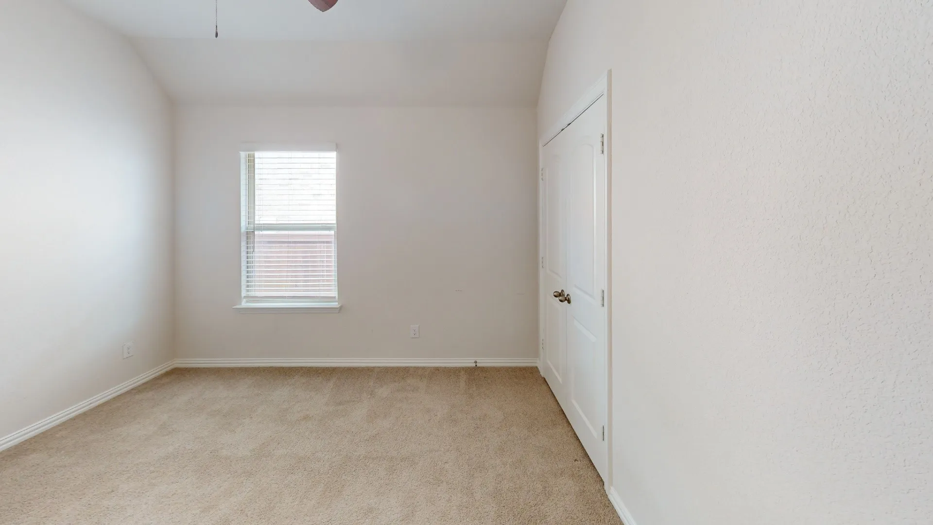 Carpeted room featuring a single window with blinds, a white door with brass hardware, a ceiling fan, and textured walls