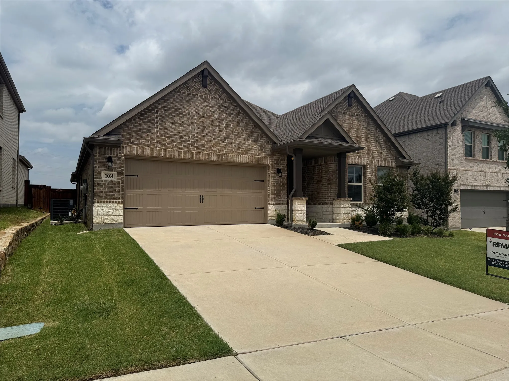 Brick Colonial home featuring a two-car attached garage, concrete driveway, and manicured front lawn with established landscaping