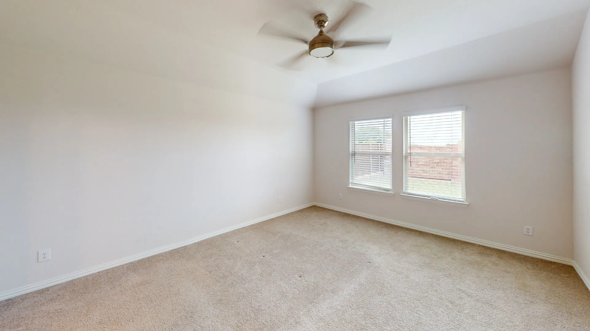 Carpeted room with a vaulted ceiling, two windows featuring blinds, and a ceiling fan