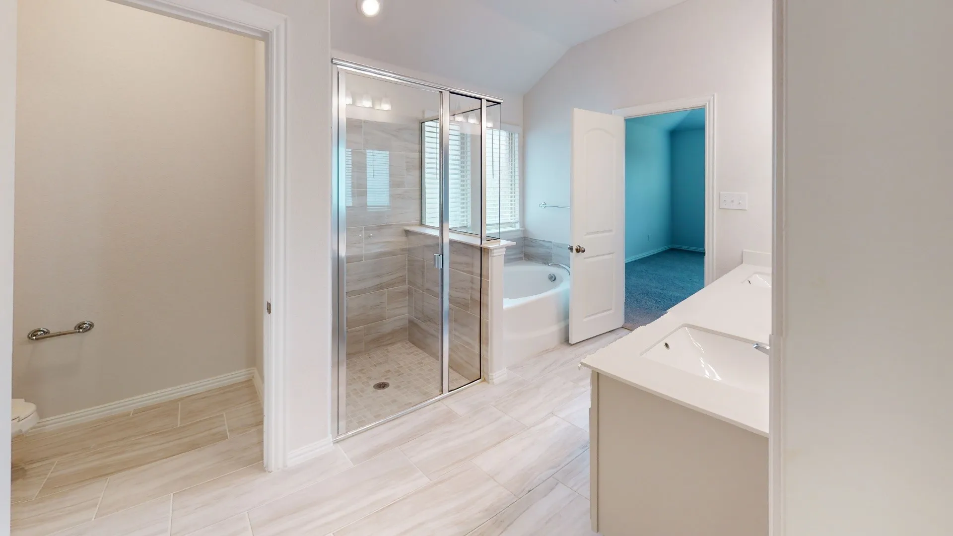 Spacious bathroom with vaulted ceiling, dual vanity, glass-enclosed shower with tile surround, separate soaking tub, and tile flooring