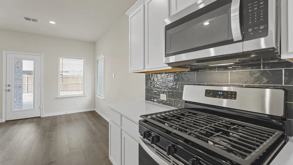 Modern kitchen featuring stainless steel appliances, crisp white cabinetry, a dark subway tile backsplash, light countertops, and wood-finish flooring