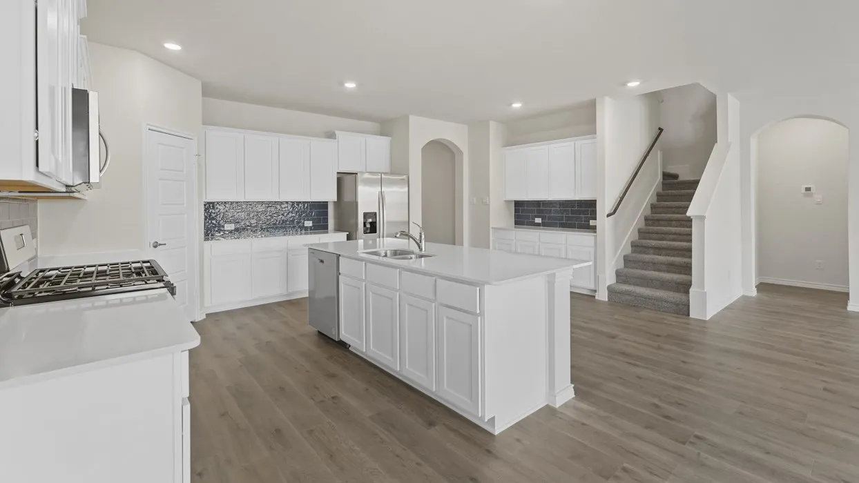 Open-concept kitchen featuring an island with an integrated sink, stainless steel appliances, white cabinetry, and wood-finish flooring