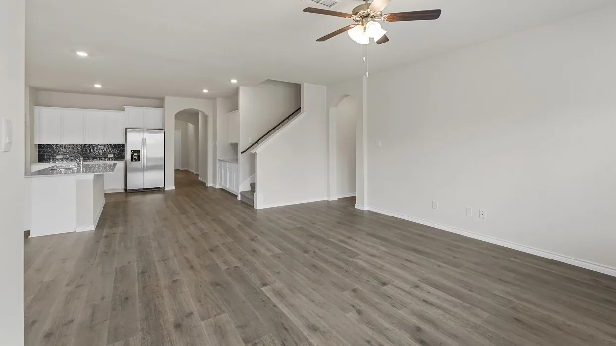 Open-concept living space featuring wood-finish flooring, a contemporary kitchen with white cabinetry, a mosaic tile backsplash, stainless steel appliances, and a central island with a sink