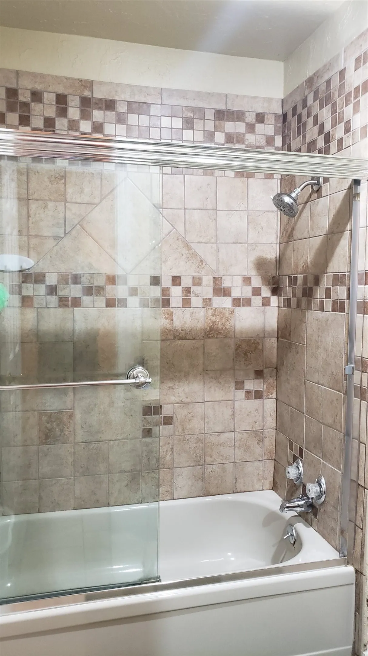 Bathtub with ceramic tile surround, integrated showerhead, and sliding glass shower door