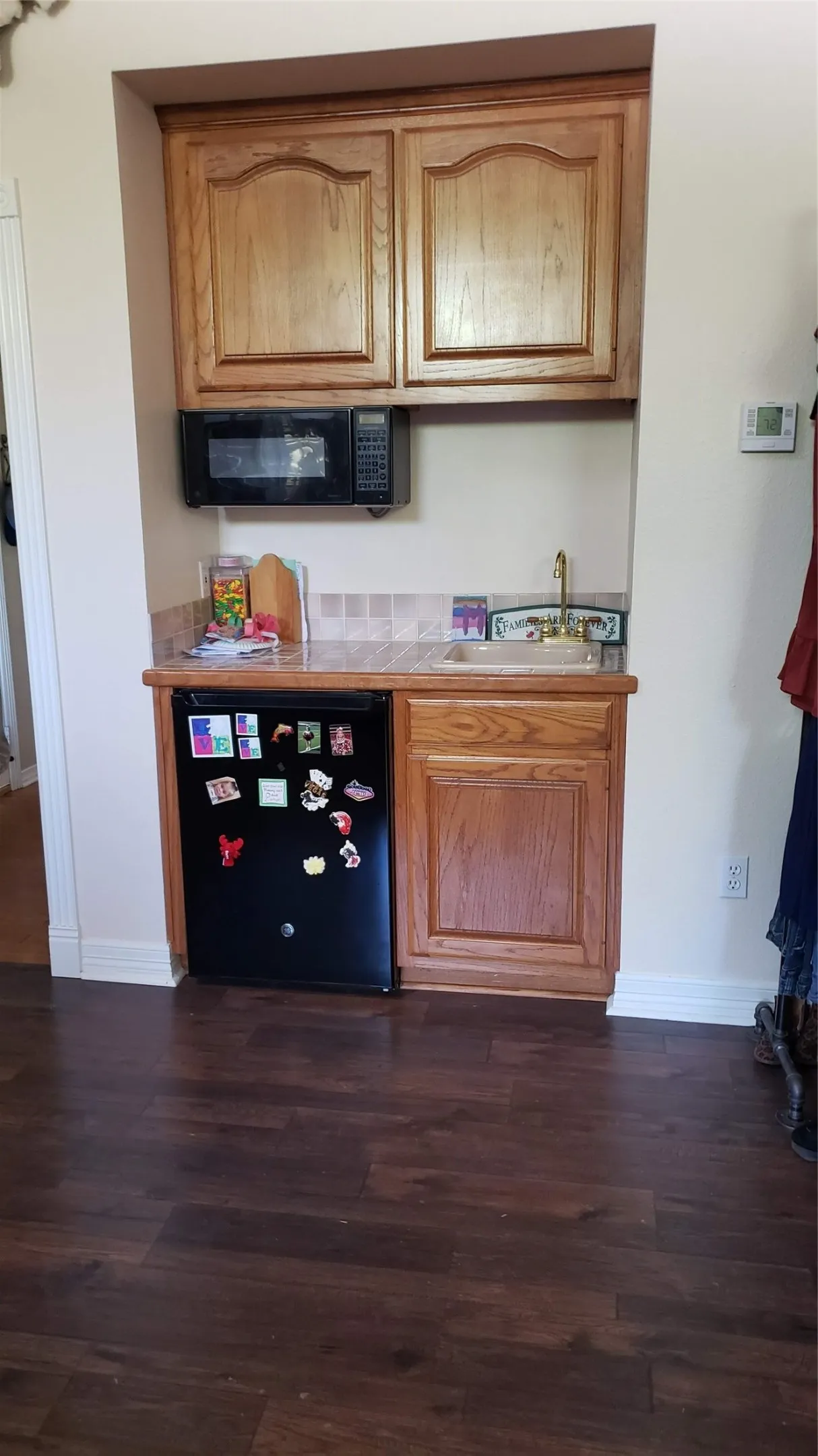 Compact kitchenette with, a built-in microwave, a sink with brass-finish faucet, and wood-finish flooring in primary