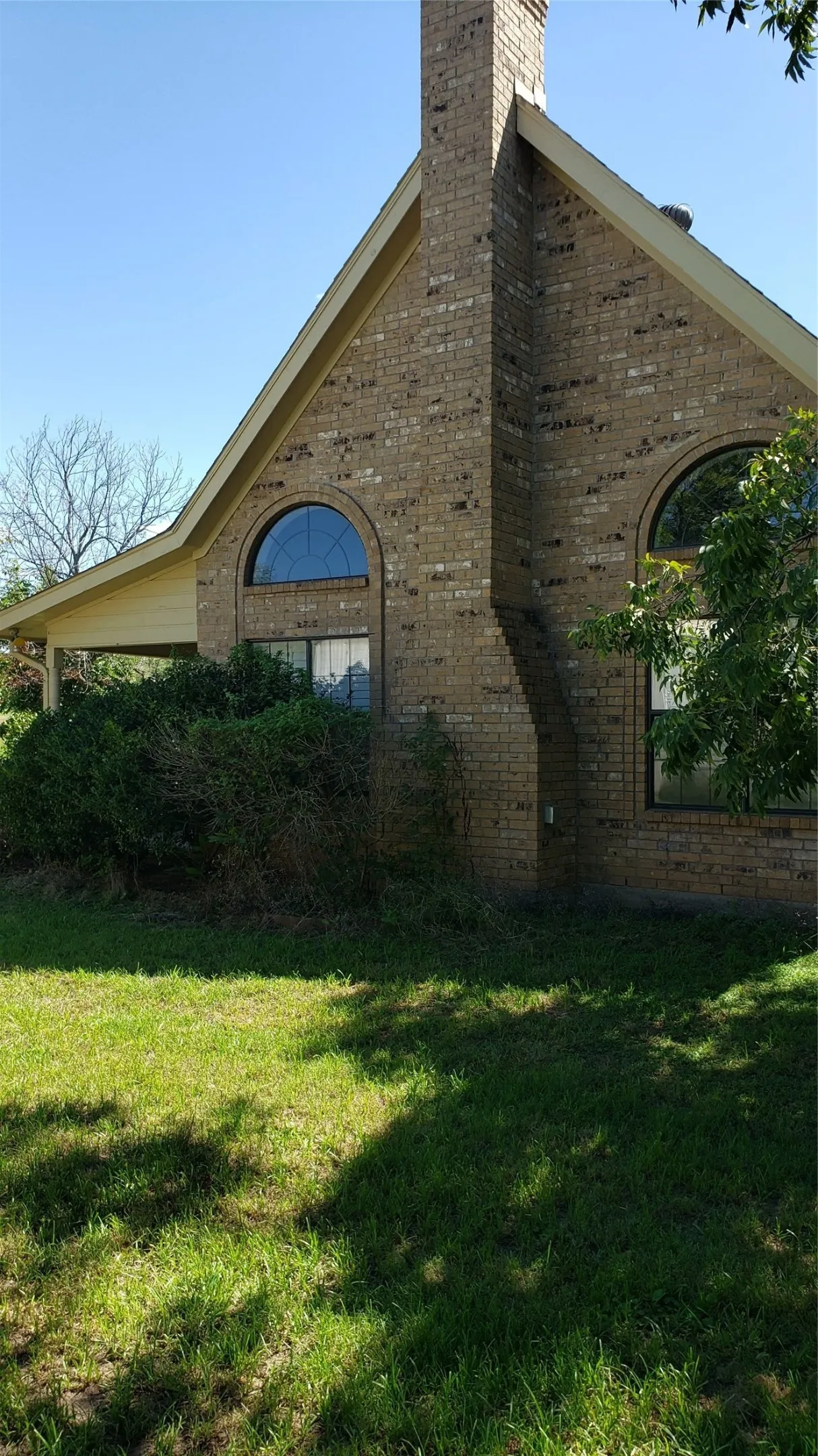 Brick exterior with prominent chimney stack, arched windows, and an extended covered patio