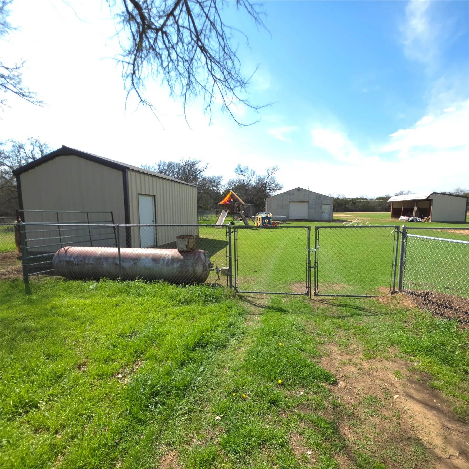 Chain link fencing with double gates leading to a Barn, Storage building and large open fron shed