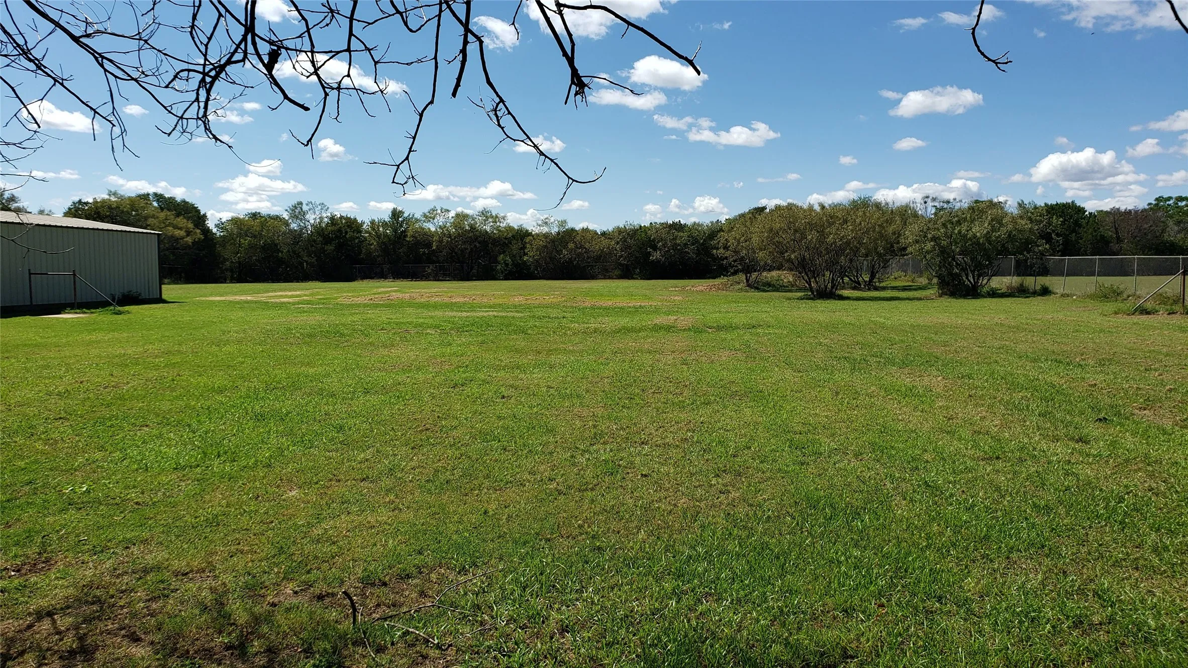 Expansive grass acreage with mature trees and a metal outbuilding