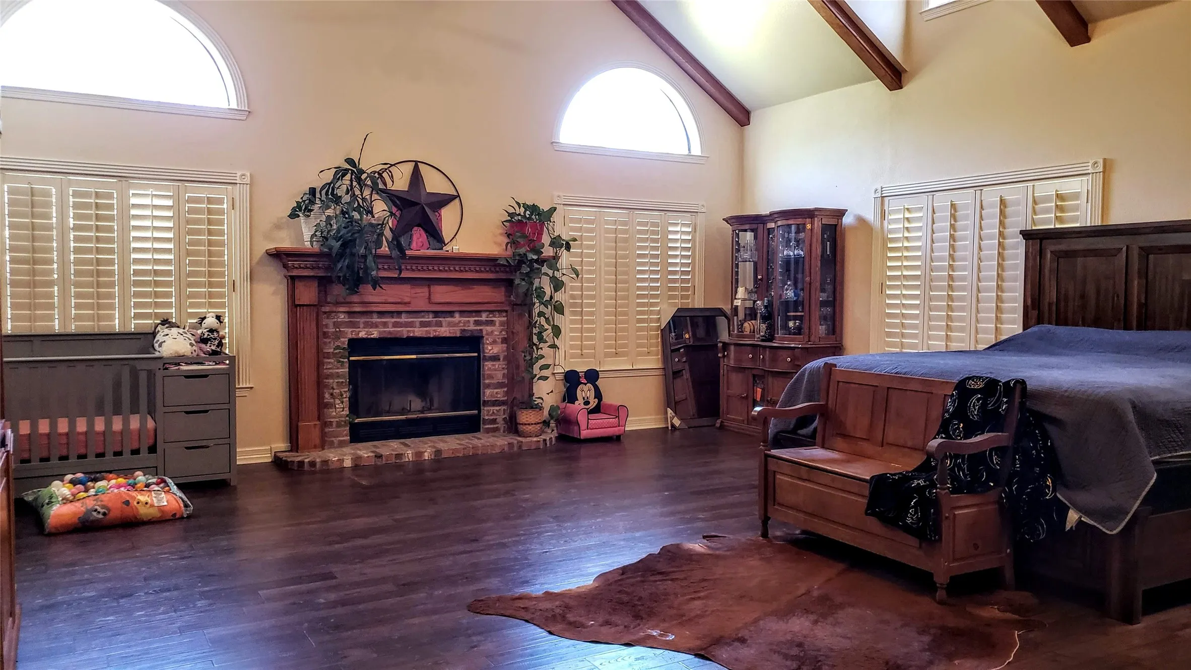 APPROX 28'X21' with Vaulted ceiling with exposed wood beams, brick fireplace with wood mantel, arched transom windows, plantation shutters, and dark wood-finish flooring