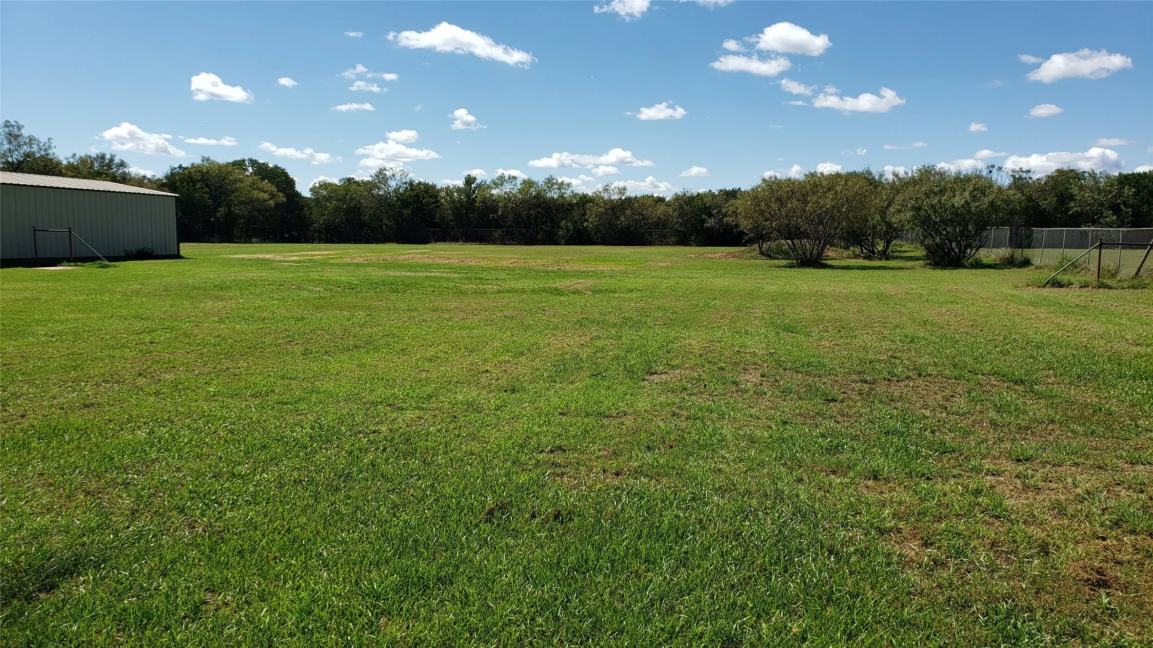 Expansive green lawn with a metal outbuilding, scattered trees, and a perimeter fence