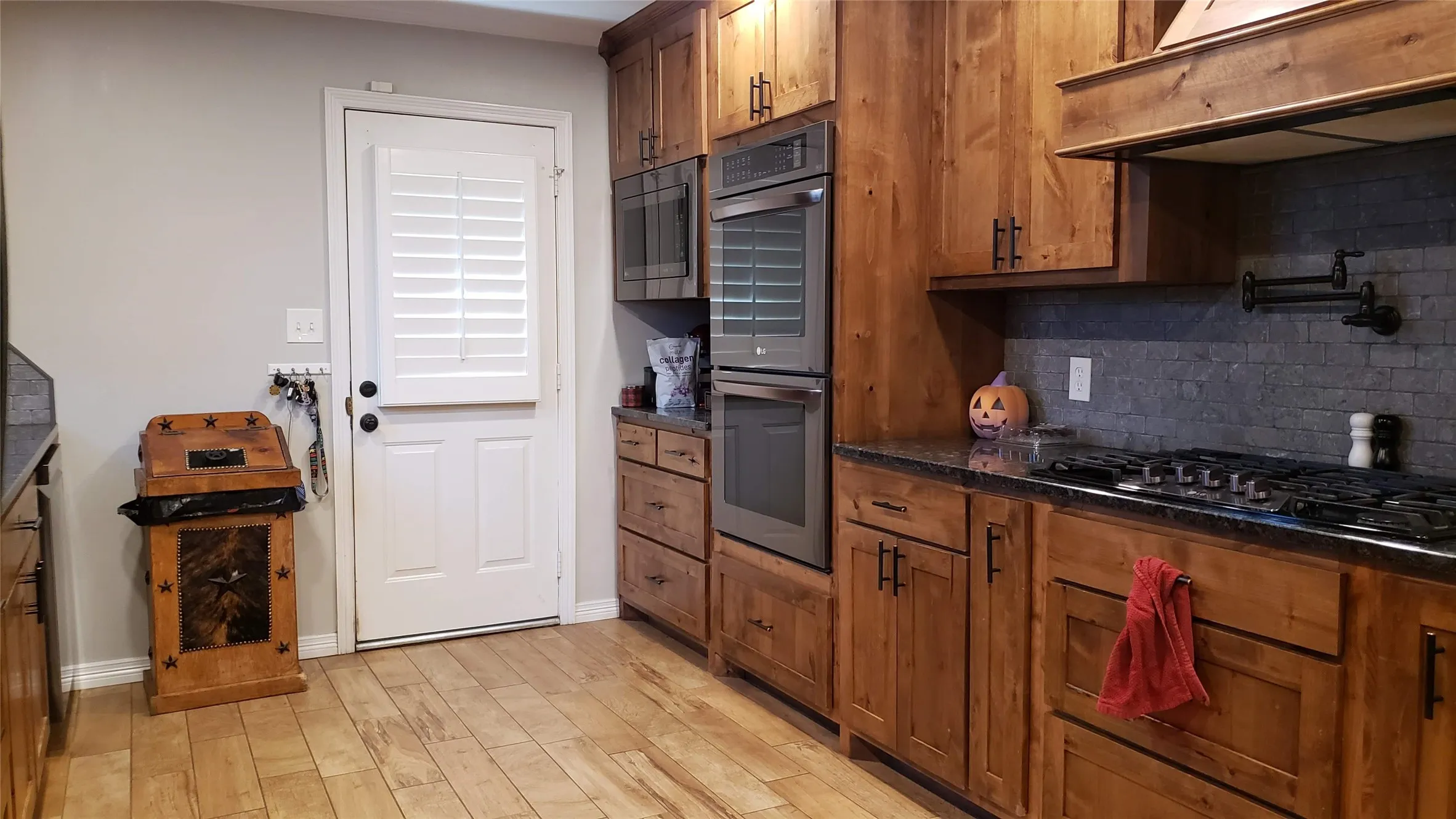 Wood-finish flooring, custom wood cabinetry, stainless steel double wall oven, gas cooktop, and dark tile backsplash