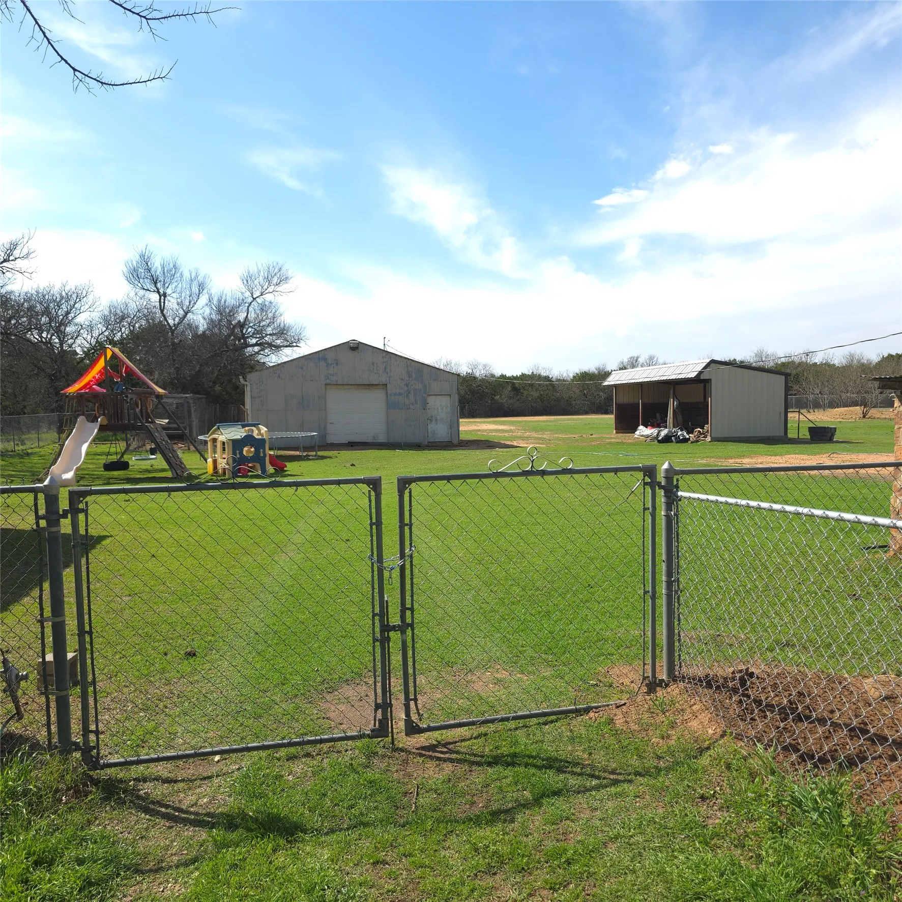 Expansive fenced yard featuring a large utility building with an overhead door, a separate open-sided structure, and a clear grassy area