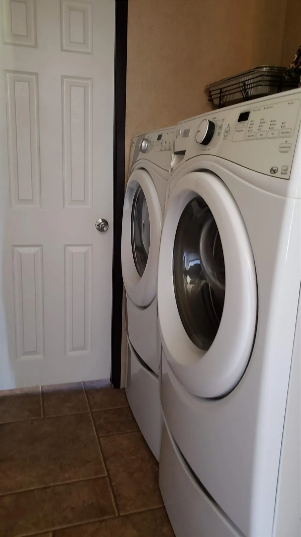 Tile flooring in a neutral tone, white paneled door, and a dedicated laundry area