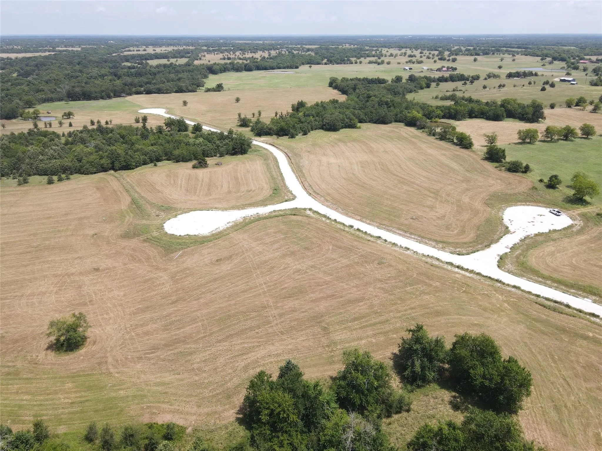 Expansive undeveloped land featuring a gravel road system, multiple building sites, and scattered mature trees