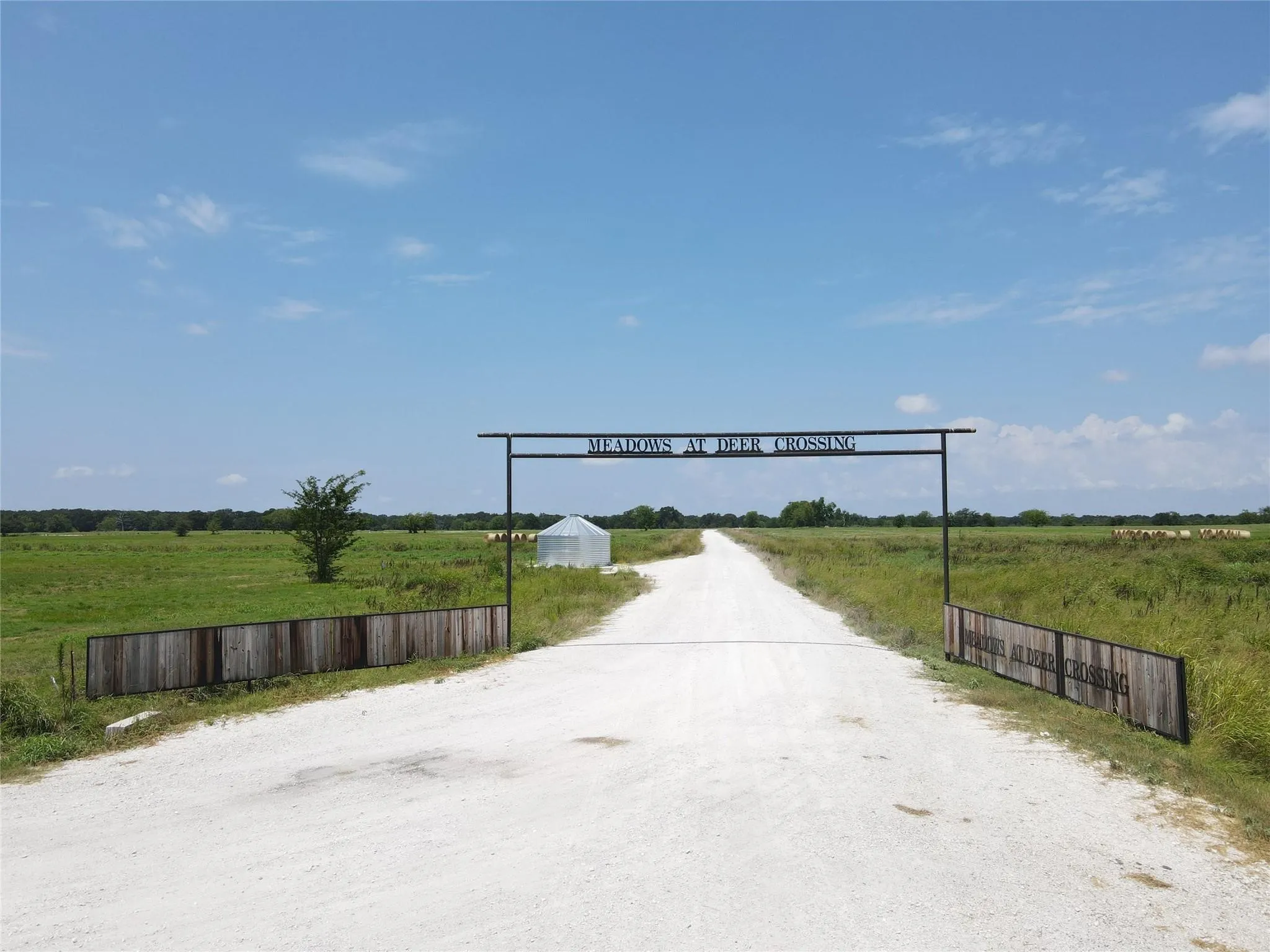 Gravel road entry with a metal archway and wood-paneled fencing