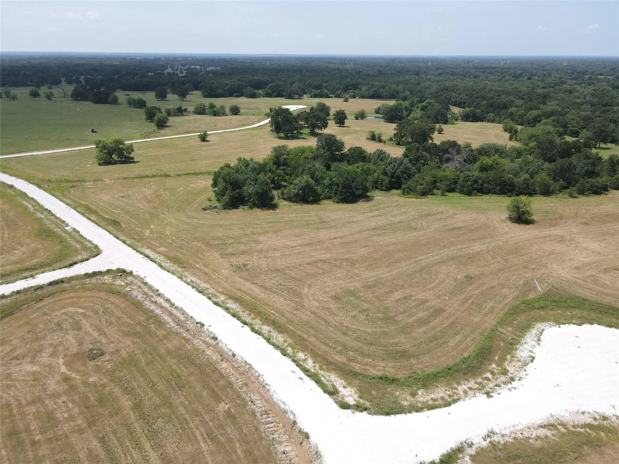 Expansive land parcel featuring existing gravel roads and scattered mature trees