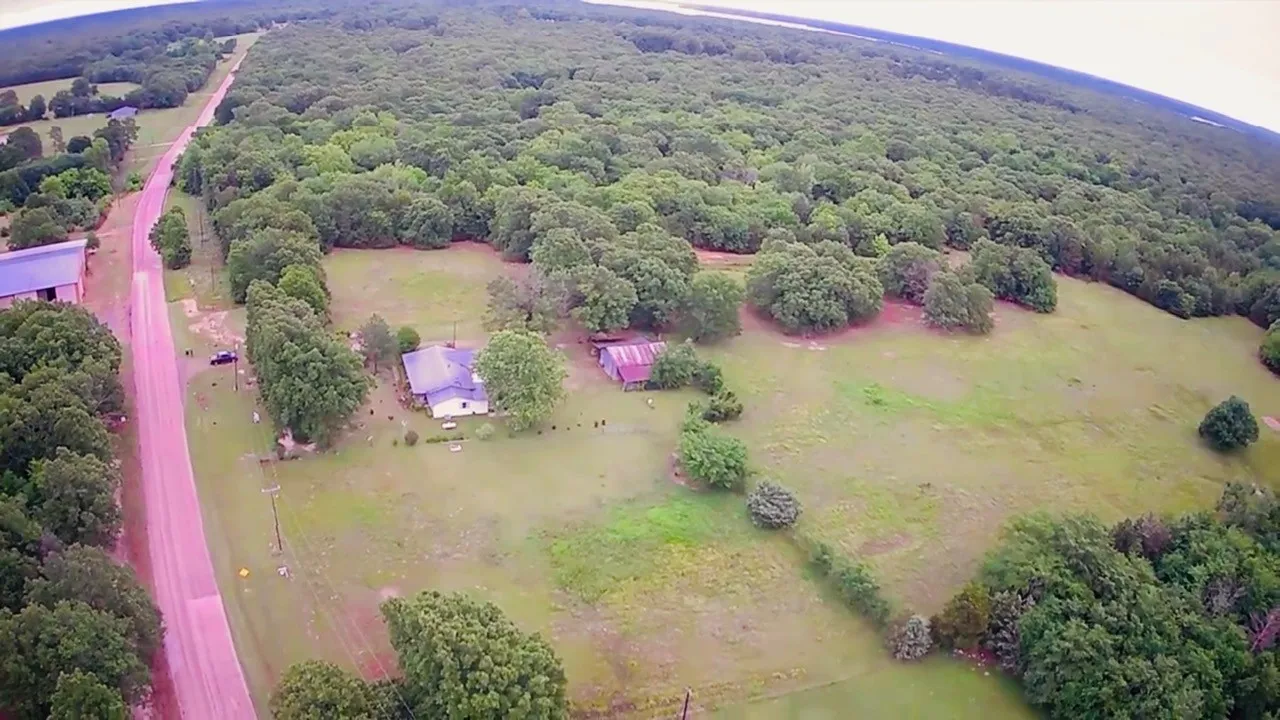 Expansive property featuring a single-story residence, a secondary structure, abundant mature trees, and a substantial portion of open land