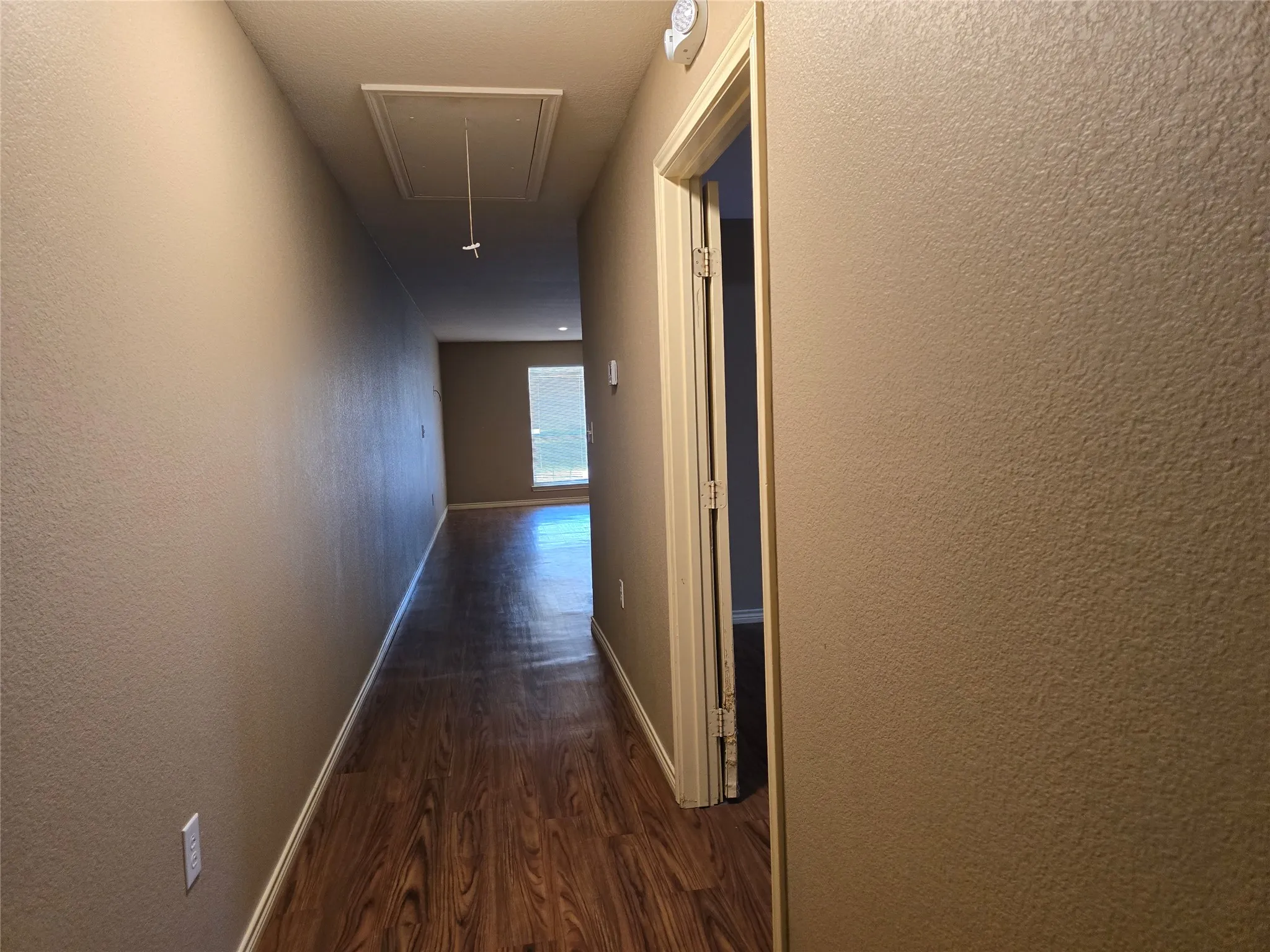 Wood-finish flooring throughout the hallway, leading to a sunlit area with a large window