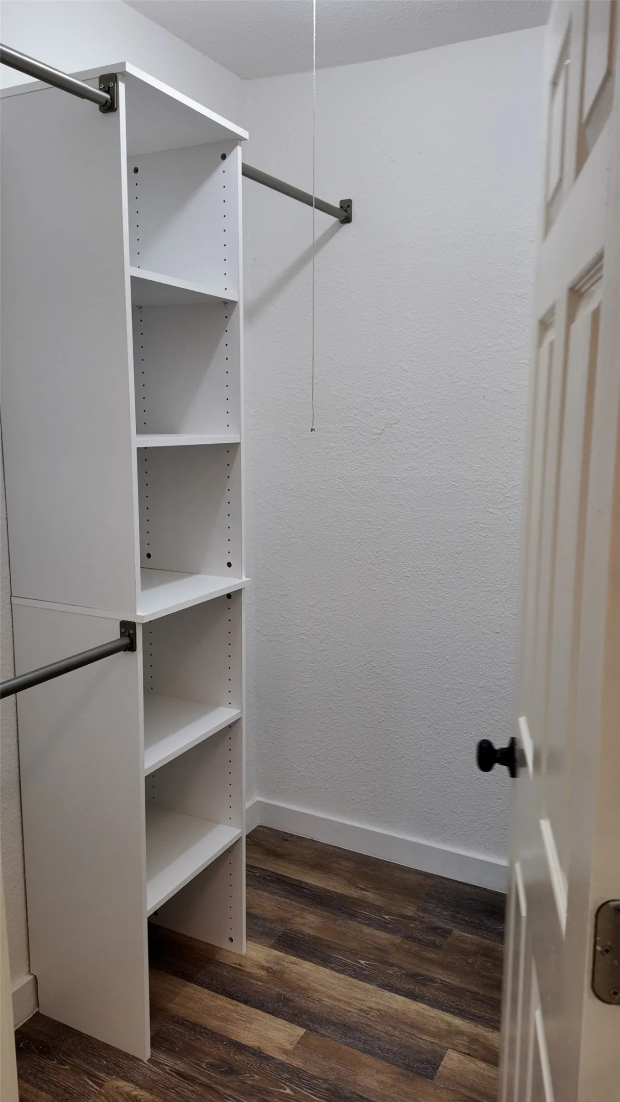 Custom shelving system with adjustable white shelves, multiple hanging rods, and wood-finish flooring