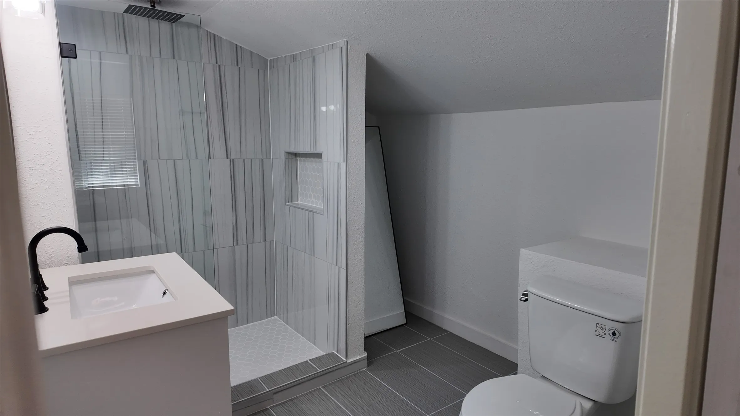Walk-in shower with glass enclosure, vertical-patterned wall tiles, and built-in niche